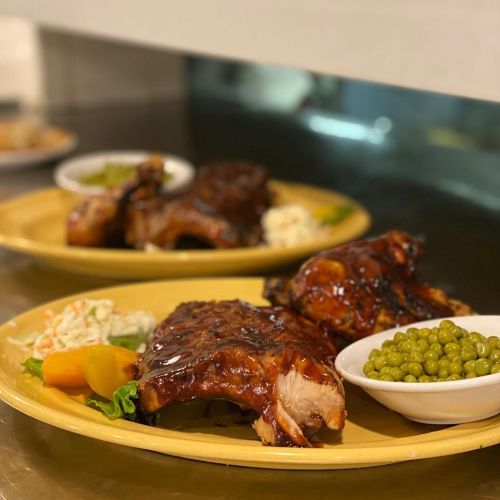 Two plates of glazed ribs served with coleslaw, peas, and mixed vegetables on a yellow platter.