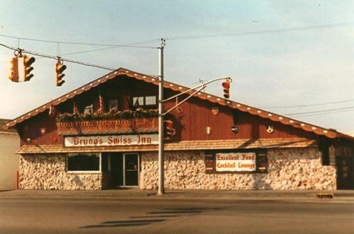 A vintage building with a sloped roof, featuring a sign for "Bruno's Swiss Inn" and traffic lights in the foreground.