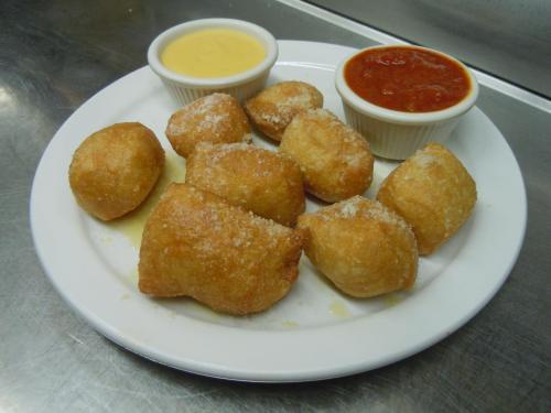 A plate of golden-brown fried dough balls, sprinkled with sugar, served with two dipping sauces: yellow and red.