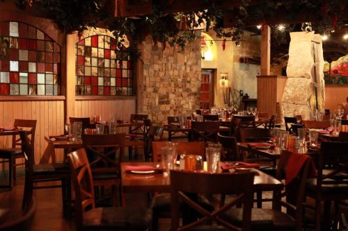 Cozy restaurant interior with wooden tables, chairs, and colorful stained glass windows. Warm, inviting atmosphere.