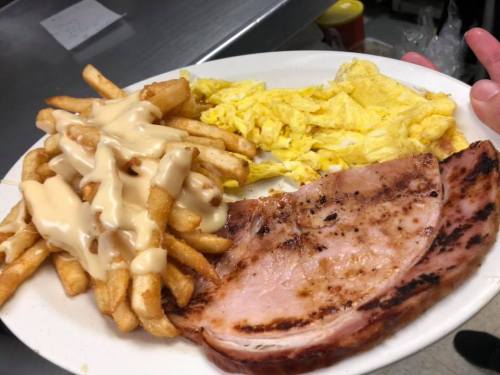 A plate with golden fries topped with sauce, scrambled eggs, and a slice of grilled ham.