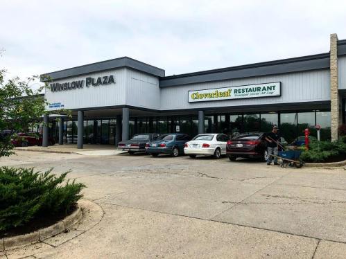 Exterior view of Winslow Plaza featuring Cloverleaf Restaurant, with parked cars and a person pushing a cart.