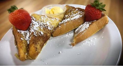 Three slices of French toast topped with strawberries and powdered sugar, served with a side of butter.