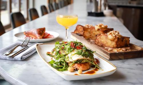 A beautifully plated dish with greens and fish, accompanied by a cocktail and dessert on a marble table.