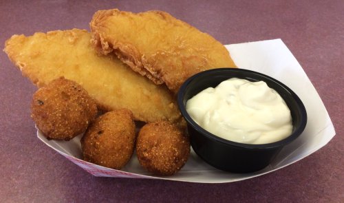 A serving of two fried fish fillets, three hushpuppies, and a cup of tartar sauce on a paper tray.