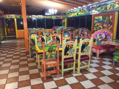 Colorful restaurant interior with vibrant, hand-painted chairs and tables, featuring a tiled floor and large windows.