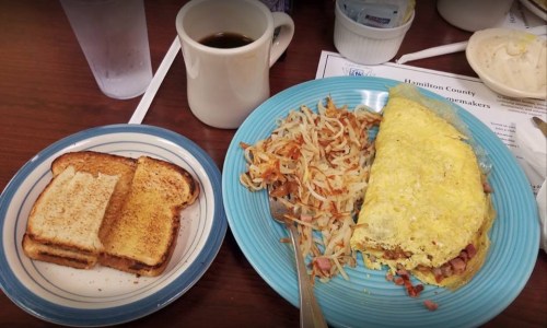 A plate with a fluffy omelet, hash browns, and toast, alongside a cup of coffee and a glass of water.