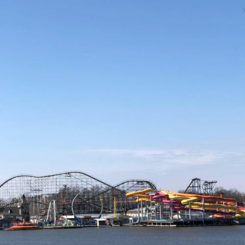 A view of a theme park featuring a roller coaster and colorful water slides against a clear blue sky.