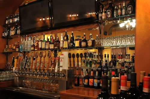 A well-stocked bar featuring various bottles of liquor, beer taps, and glasses on shelves against a warm backdrop.