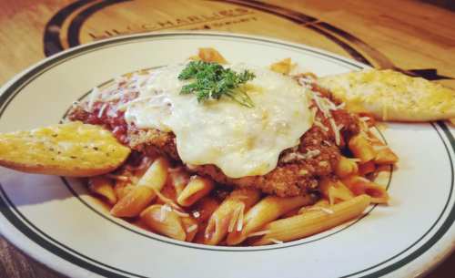 A plate of pasta topped with breaded chicken, marinara sauce, melted cheese, and garlic bread on the side.