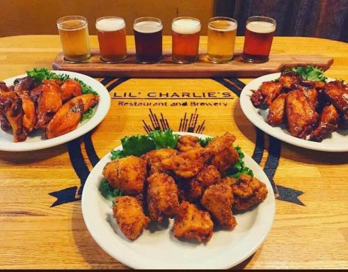 A wooden table with three plates of chicken wings and a flight of craft beers in the background.