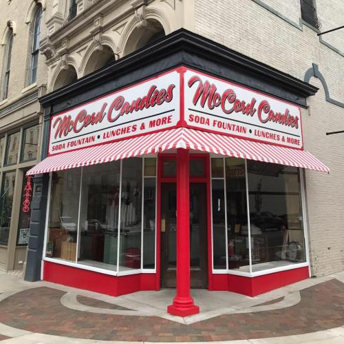 A vintage-style candy shop with a red and white striped awning, featuring large windows and a welcoming entrance.
