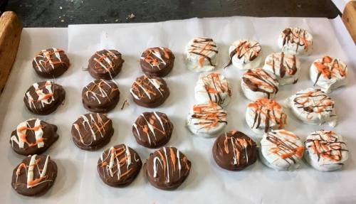 A tray of round cookies, half covered in chocolate and half in white icing, drizzled with orange and white stripes.