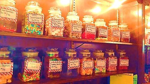 A colorful display of jars filled with various candies, each labeled with prices, on a wooden shelf.