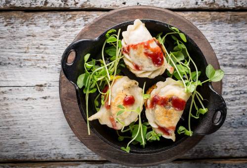 Three dumplings drizzled with sauce, served on a bed of fresh greens in a small cast iron skillet.