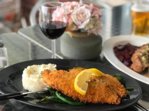 A plate of crispy fish with lemon, served with mashed potatoes and green beans, alongside a glass of red wine.