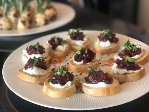 A platter of toasted bread slices topped with cream cheese, red onion jam, and fresh herbs.