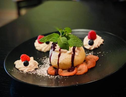 A dessert plate featuring a baked apple with sauce, surrounded by whipped cream, raspberries, and blueberries.