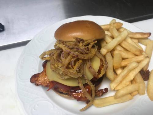 A burger topped with fried onions and pickles, served with a side of golden French fries on a white plate.