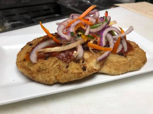 A plate of two toasted flatbreads topped with colorful pickled vegetables and a savory sauce.