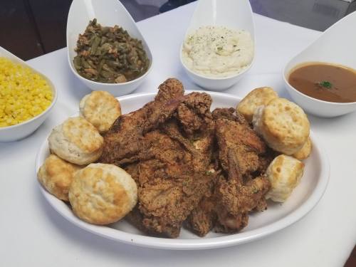 A platter of fried chicken surrounded by biscuits, with bowls of green beans, mashed potatoes, and corn in the background.
