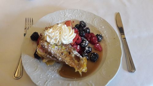 A plate of French toast topped with whipped cream and mixed berries, drizzled with syrup and dusted with powdered sugar.