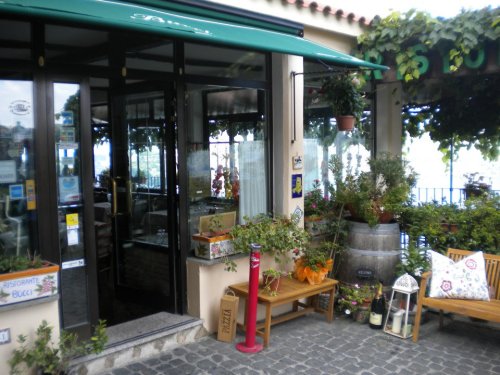 A charming restaurant entrance with plants, outdoor seating, and a view of the water, featuring a green awning.