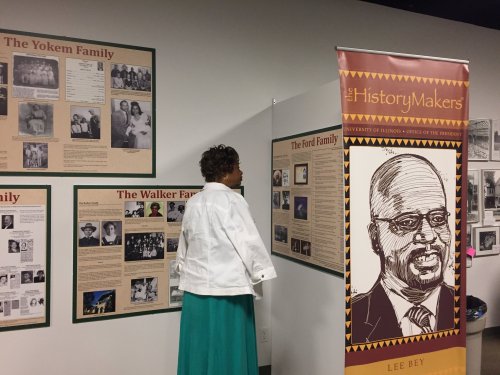 A woman in a white jacket examines historical displays about families at a museum, with a banner for The HistoryMakers.