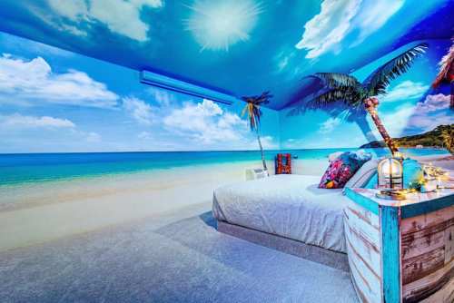 A beach-themed bedroom with a mural of ocean and palm trees, featuring a cozy bed and decorative accents.