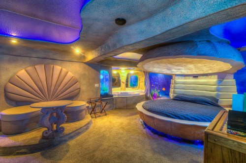 A unique underwater-themed bedroom with blue lighting, a round bed, and aquatic decor, creating a whimsical atmosphere.