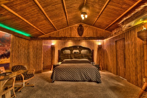 Cozy, tropical-themed bedroom with bamboo walls, a stone headboard, and warm lighting.