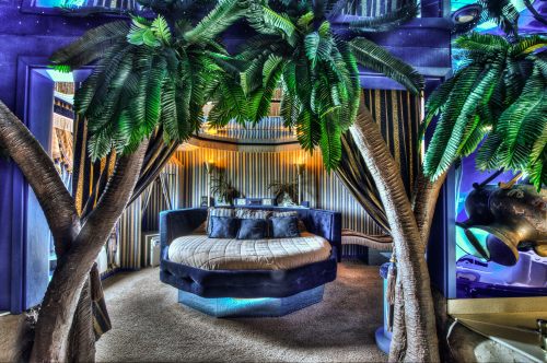 A luxurious bedroom with a round bed, surrounded by palm trees and soft lighting, creating a tropical ambiance.