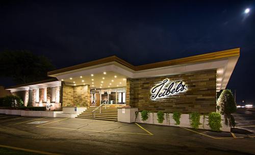 A modern restaurant exterior at night, featuring stone walls, bright lights, and a prominent sign reading "Teibel's."