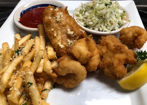 A plate of fried seafood, including shrimp and fish, served with fries, coleslaw, and a side of ketchup.