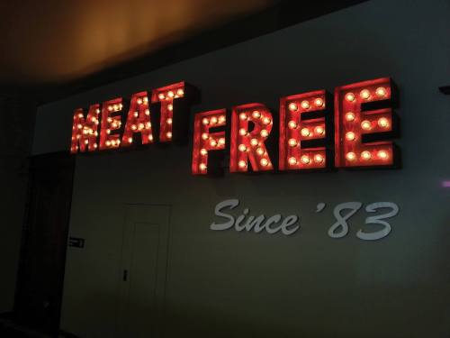 Brightly lit sign reading "MEAT FREE" with "Since '83" below it, displayed on a wall.