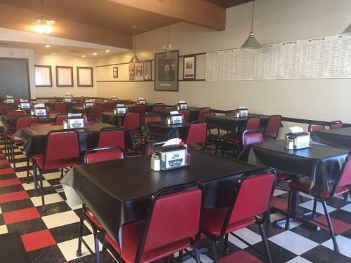 A spacious restaurant interior with red and black checkered floors, empty tables, and a menu board on the wall.