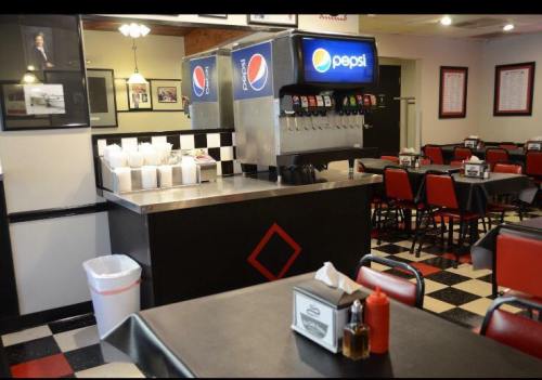A diner interior featuring a Pepsi soda fountain, red and black decor, and empty tables with checkered flooring.
