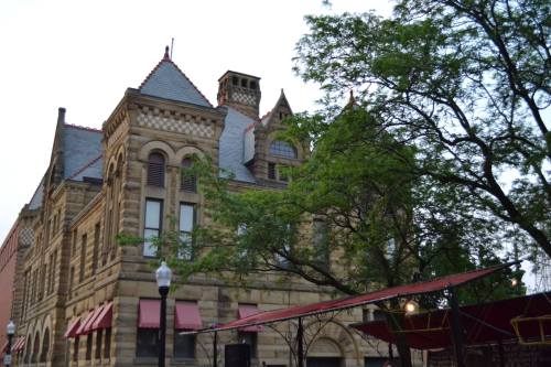 Historic stone building with ornate architecture, red awnings, and surrounding trees.