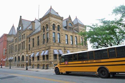 Historic stone building with a school bus parked in front, featuring striped awnings and a tree nearby.