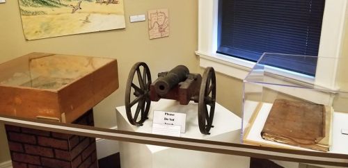 A historic cannon displayed in a museum, surrounded by glass cases and informational signs.