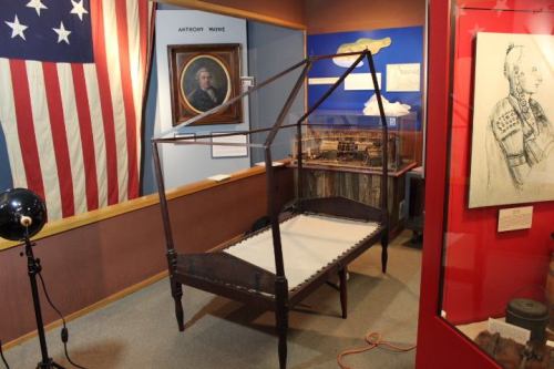 A historical exhibit featuring a wooden bed frame, an American flag, and various artifacts on display in a museum.