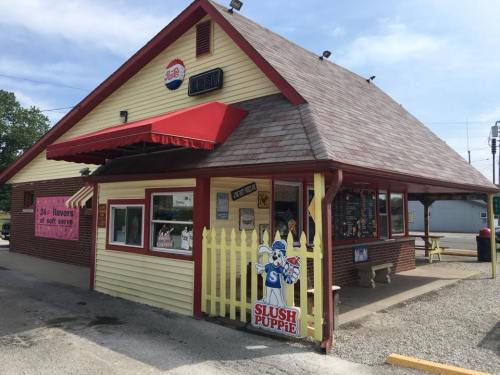 A colorful ice cream shop with a slush puppy sign, featuring a red awning and a yellow picket fence.