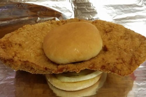 A large, crispy fried chicken fillet topped with a soft bun, resting on a bottom burger bun with onion slices.