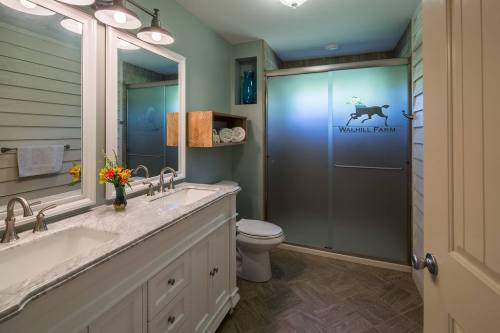 Modern bathroom with a double sink, large mirror, and frosted glass shower door featuring a farm logo.
