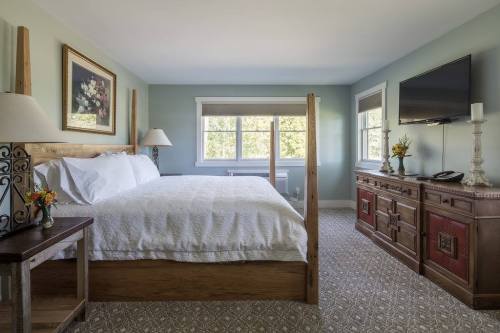 Cozy bedroom with a four-poster bed, floral artwork, a TV, and a wooden dresser, featuring soft blue walls and natural light.