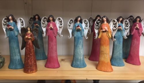 A collection of decorative angel figurines in various colors and styles, arranged on a wooden shelf.