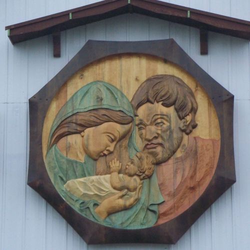 Carved wooden relief depicting Mary, Joseph, and baby Jesus in a tender moment, framed in an octagonal shape.