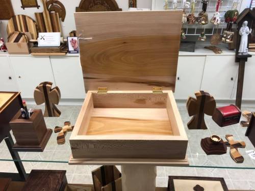 A wooden box with a hinged lid, displayed on a table among various wooden crafts and decorations.