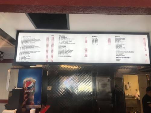 Menu board displaying various food items including sandwiches, salads, wings, sides, and dessert drinks.