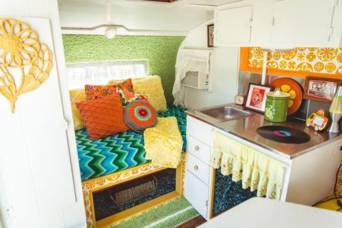 Cozy retro camper interior with colorful cushions, green walls, and a small kitchen area featuring a sink and decor.